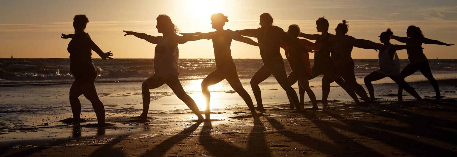 group of people doing yoga on beach at sunset