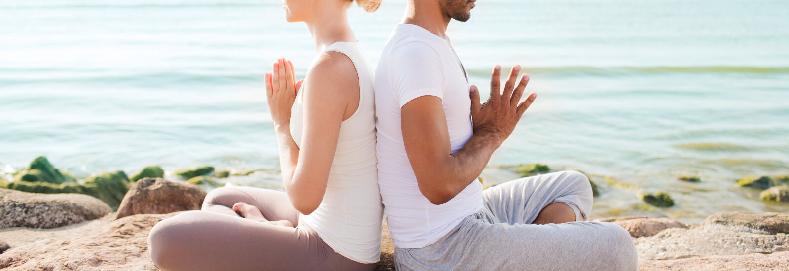 couple doing yoga on rock by water