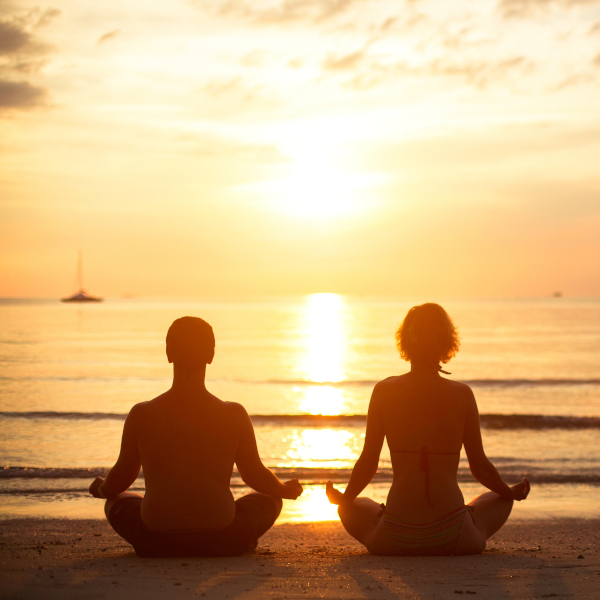 couple meditating on beach at sunrise